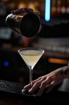 male barman hands is making cocktail with steel shaker at the bar counter, close-up