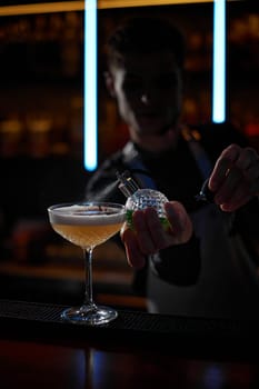 barman splashing absinthe from siphon on glass of cocktail
