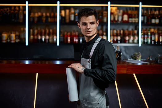 Handsome barman in apron standing at the bar counter