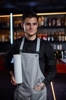 Handsome barman in apron holding box for bottle and standing at the bar counter