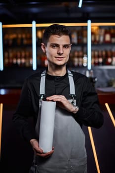 Handsome barman in apron holding box for bottle and standing at the bar counter