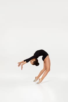 modern style dancer on studio background. little gymnast girl in black sportswear performs gymnastic poses.