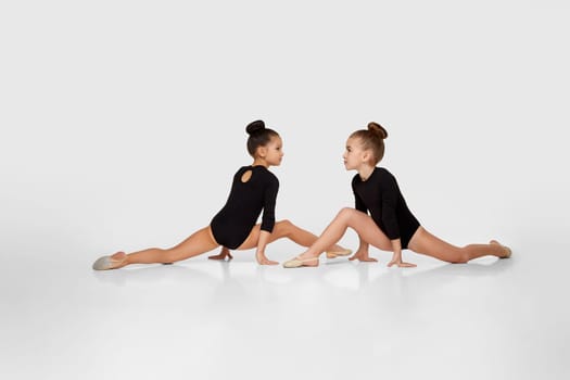 two young beautiful gymnast girls in black sportswear performs gymnastic poses