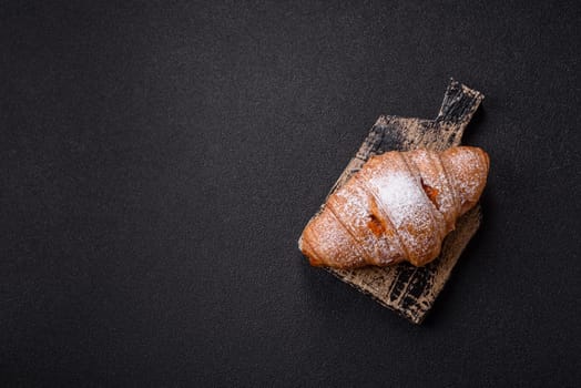 Sweet fresh crispy croissant with fruit filling on a dark concrete background