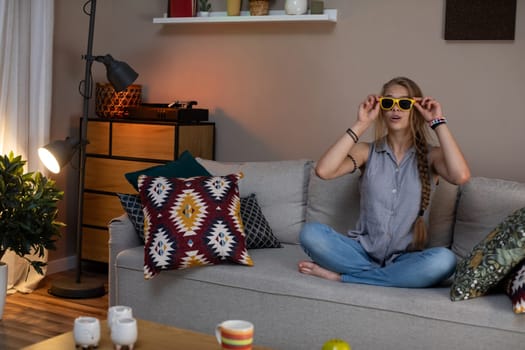 A young woman is comfortably relaxing on her sofa, wearing stylish sunglasses while enjoying her cheerful living space