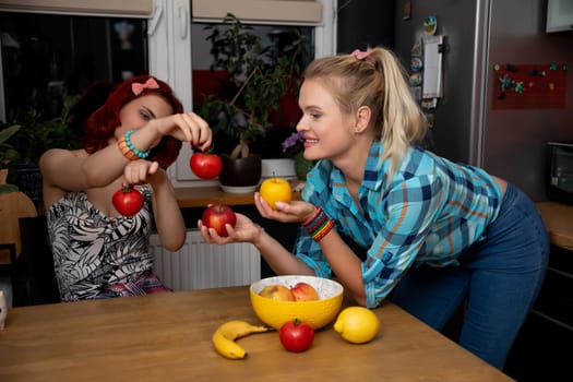 Two friends are playfully interacting and having fun with colorful fresh fruits in a warm kitchen atmosphere