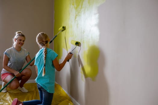 Children are collaborating on a painting project at home, with a bright yellow wall enhancing creativity