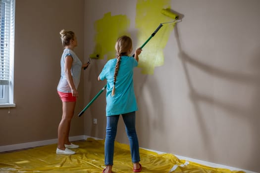 Two people joyfully paint a wall bright yellow in a cozy living room, showcasing creativity and collaboration