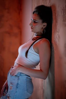 A stylish young woman confidently poses elegantly against a textured wall while wearing a trendy outfit
