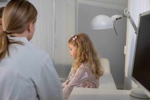 In a bright and contemporary workspace, a young girl is sitting at a desk while an adult is nearby, supporting her