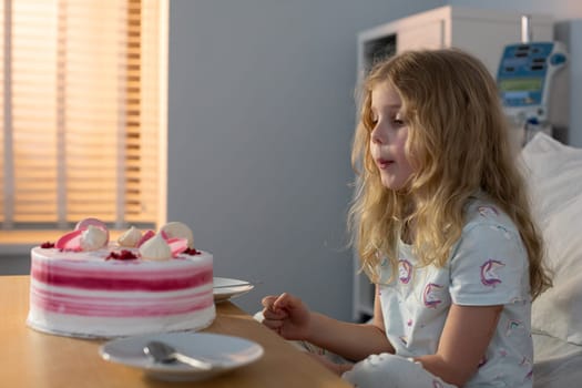 A young girl happily enjoys her birthday cake in a hospital setting, radiating pure joy and warmth to everyone around