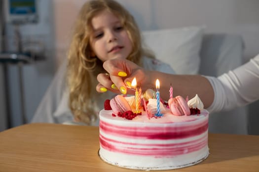 A young girl eagerly watches as beautiful candles are lit on a birthday cake, bringing joy in a hospital room