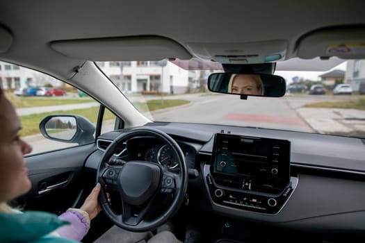 A woman is driving a modern car, showcasing advanced dashboard tech while cruising through a vibrant city street