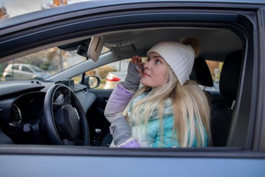A woman dressed in a warm and cozy winter outfit is seen reflecting in her car on a chilly winter day
