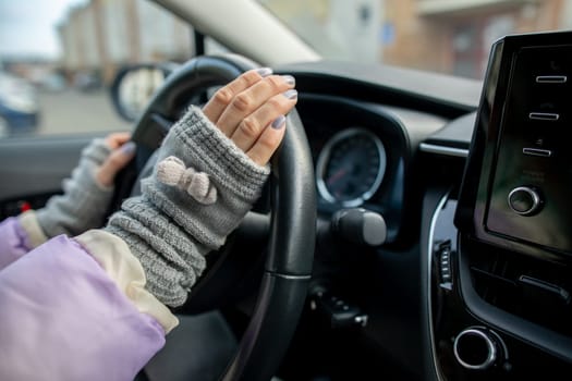 A persons hands, adorned in stylish fingerless gloves, firmly grip the steering wheel of a car while driving