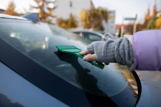 A person diligently using a scraper tool to clean a cars windshield while enjoying the beautiful autumn sunlight