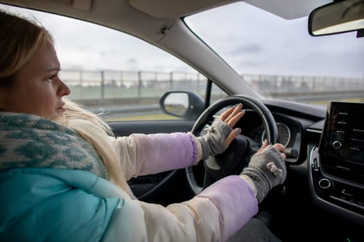 A young woman is driving in winter conditions, staying focused while wearing warm clothing and a pair of gloves