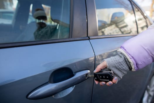 A person is unlocking a car door using a key fob in a winter setting, showcasing convenience and modern technology