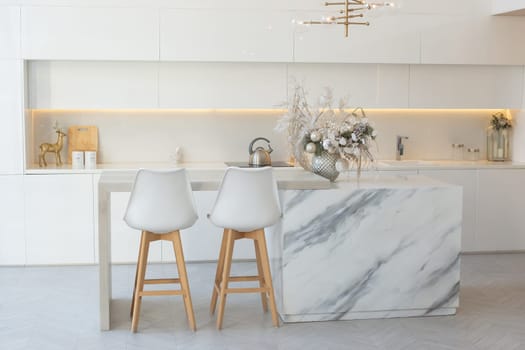 Kitchen with white interior, marble table in the middle, silver Christmas decorations