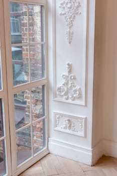 Elegant white interior with ornate wall molding and large window overlooking brick building.
