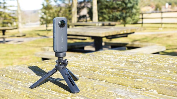 Black Tripod with Insta360 Camera Positioned on a Table in a Scenic Outdoor Park Setting. Syracuse NY USA - 08.02.2024.