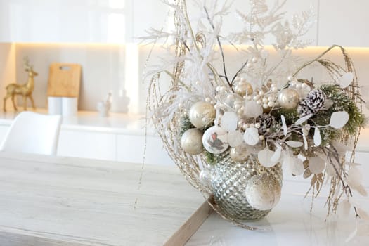 A luxury silver vase with white branches and balls stands on a table in a white kitchen interior. Close up