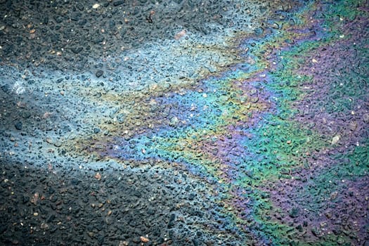 Iridescent gasoline spill creates a colorful rainbow pattern on a wet asphalt road surface