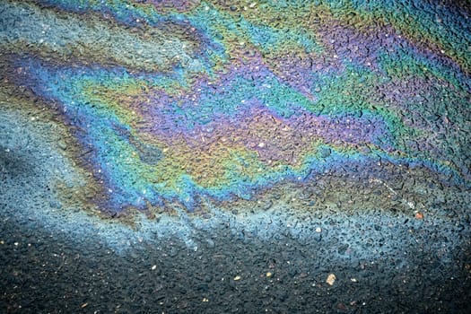 Gasoline rainbow creating colorful pattern on asphalt road