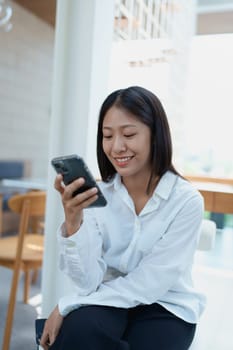 Young woman smiling while using smartphone in a modern caf setting, expressing joy and engagement with technology.