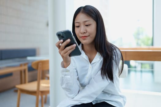 Young woman sitting indoors engaged in smartphone use while relaxing in a modern bright space.