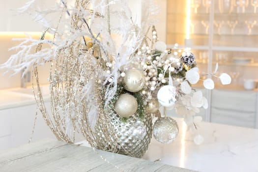 A silver vase with white branches and balls stands on a table in a white kitchen interior. Close up