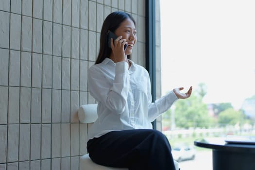 Professional woman communicating on smartphone with bright smile in modern office setting, enjoying conversation.