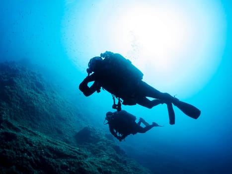 two scuba divers swimming in the ocean, one of them is looking down at the ocean floor