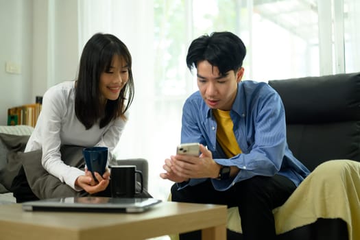 Young couple relaxing in living room and sharing social media news on mobile phone.
