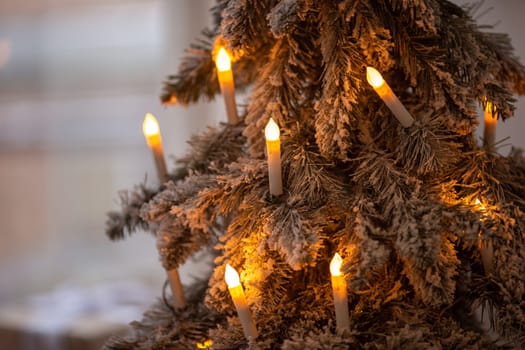 Cozy candle-lit christmas tree decor with frosted snowy branches.