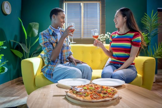 Two friends celebrate together with pizza and drinks on a cozy couch in a vibrant, colorful living room