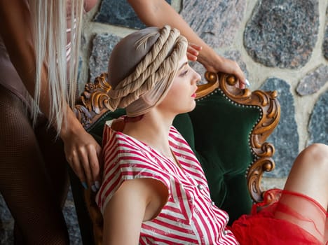 Amidst a rustic setting, a chic model showcases a stunning vintage look in a stylish chair. The soft light highlights her poised demeanor, creating an artistic atmosphere of elegance.