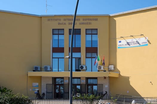 Catania, Italy - February 20, 2025: Istituto Istruzione Superiore Duca degli Abruzzi with European and Italian flags. Yellow building, parking area with cars and motorcycles. Concept: education