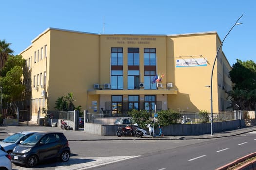 Catania, Italy - February 20, 2025: Urban scene featuring Istituto Istruzione Superiore Duca degli Abruzzi, flags, cars, motorcycles, and a scooter. Concept: educational institution