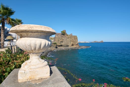 Coastal garden scene with a stone pot filled with succulents, surrounded by other planters. Blue sky and sea in the background. Concept: coastal gardening