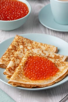 Savory crepes filled with fresh orange fish roe served on a light blue plate at a cozy breakfast table.