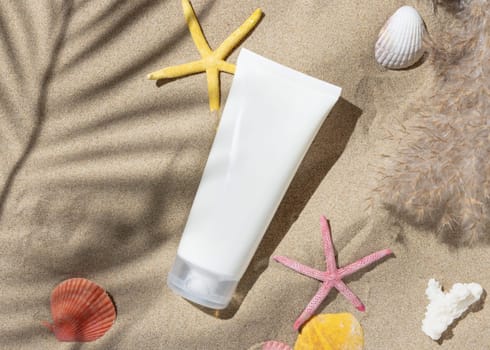 White blank cream tube, starfishes and seashells on a sandy beach top view, hard shadow. Sunscreen cosmetics mockup. Summer vacation with spf uv-protected sunbathing