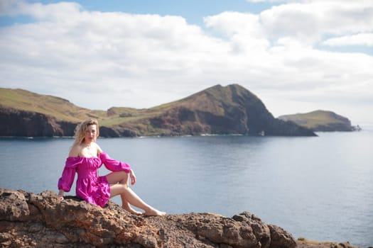 Blonde influencer wearing a pink dress sitting on a rock enjoying the landscape of ponta de s o louren o, madeira island, portugal