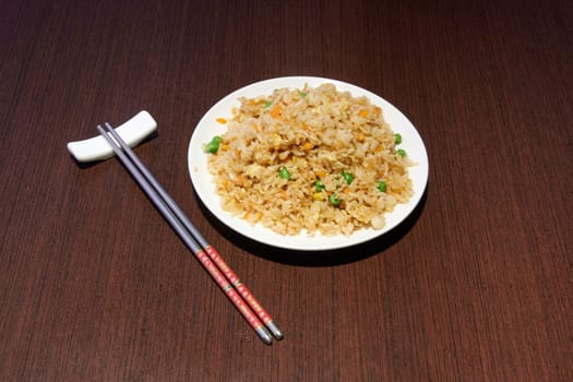 A plate of rice with chopsticks next to it. The chopsticks are red and white. The plate of rice is on a wooden table