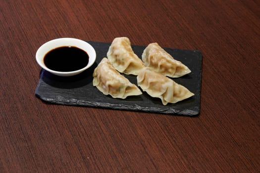 A plate of dumplings with sauce on a table. The dumplings are small and white
