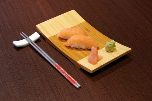 A plate of sushi with chopsticks and a small amount of wasabi. The chopsticks are red and white