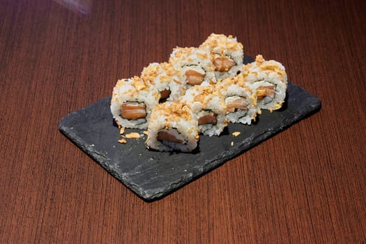 A plate of sushi with a black plate on a wooden table. The sushi is made of rice and meat