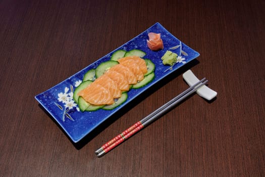 A plate of sushi with chopsticks next to it. The plate is blue and has a design of flowers on it. The chopsticks are red and are placed on the table