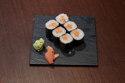 A plate of sushi with a green sauce and a piece of ginger on it. The sushi is rolled up and sitting on a black plate