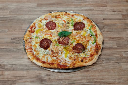A pizza with pepperoni, cheese, and basil on top. The pizza is sitting on a wooden table